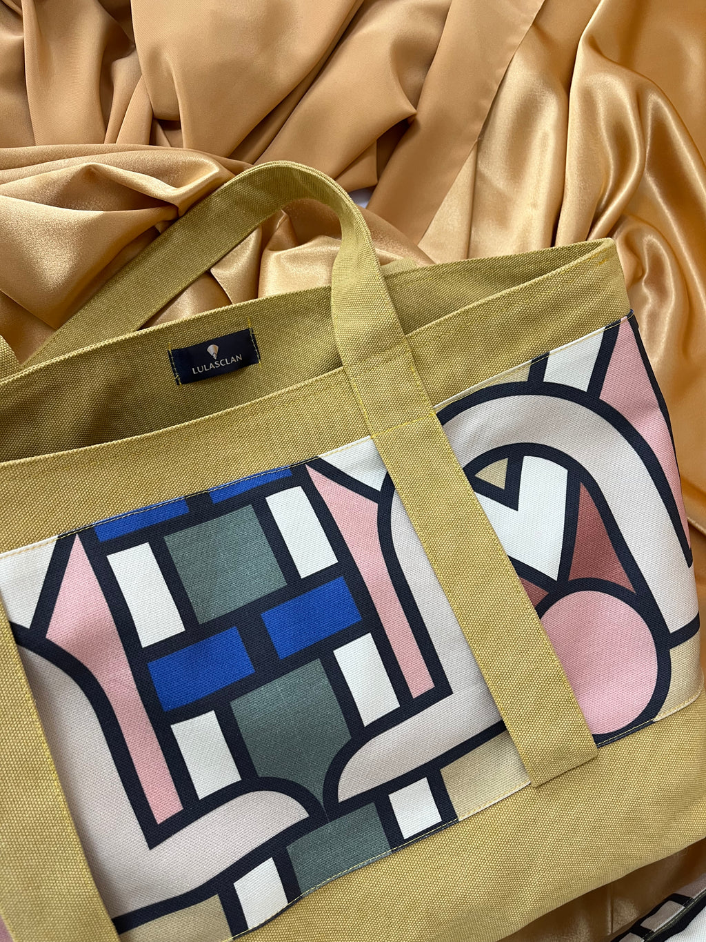 Tote bag with geometric pattern and beige handle on a satin background