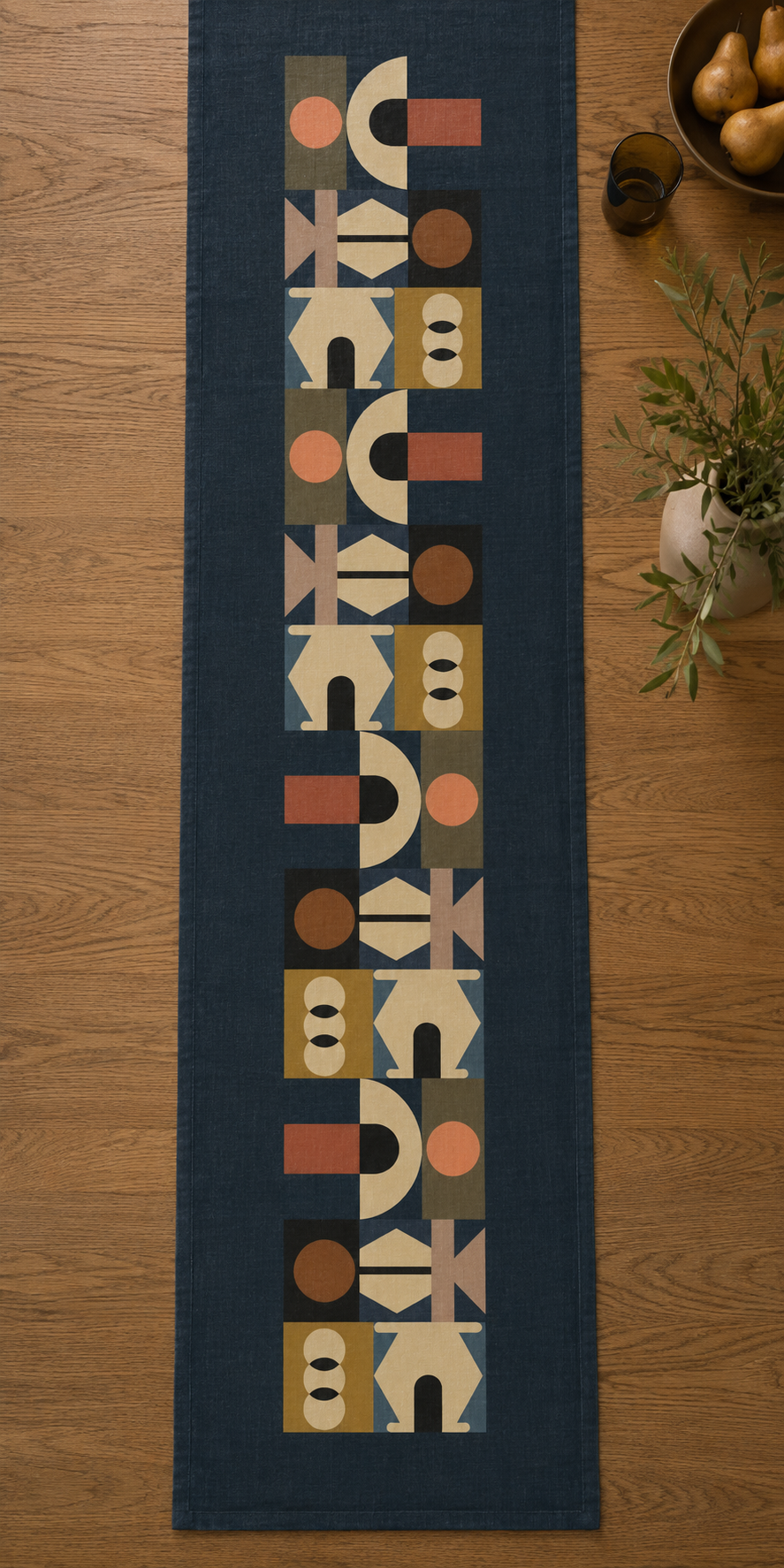 Lulasclan  The Gathering Designer Table runner navy blue runner rug with a vertical geometric pattern of beige, brown, and terracotta shapes, laid flat on a light brown wooden floor with decorative plants and fruit in the background.