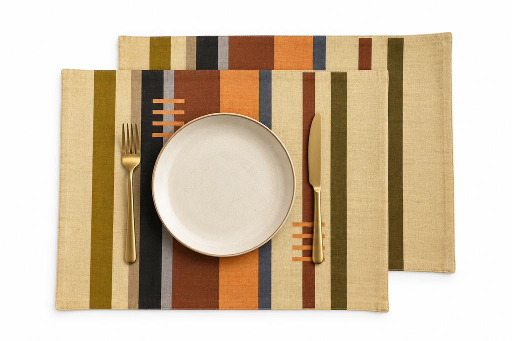 The Pastures by Lulasclan Designer  placemats are shown with striped design  in beige, brown, orange, green, and navy, styled with a white plate and gold-toned cutlery on a white background.