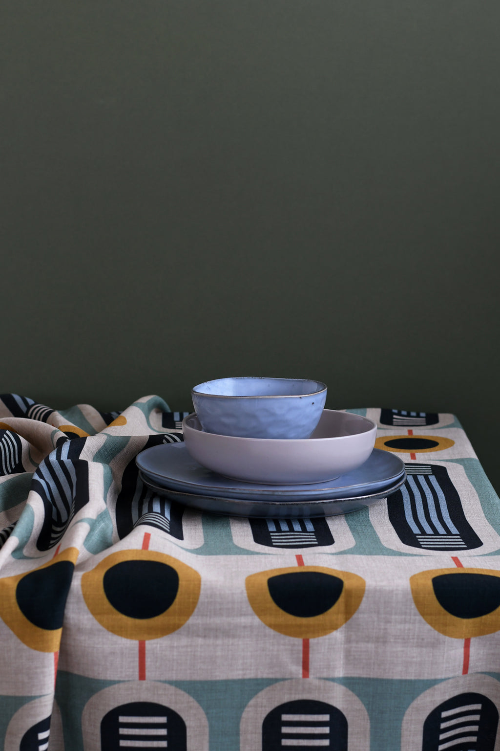 A patterned linen tablecloth on a dining table featuring a bowl and plates, with a dark background.